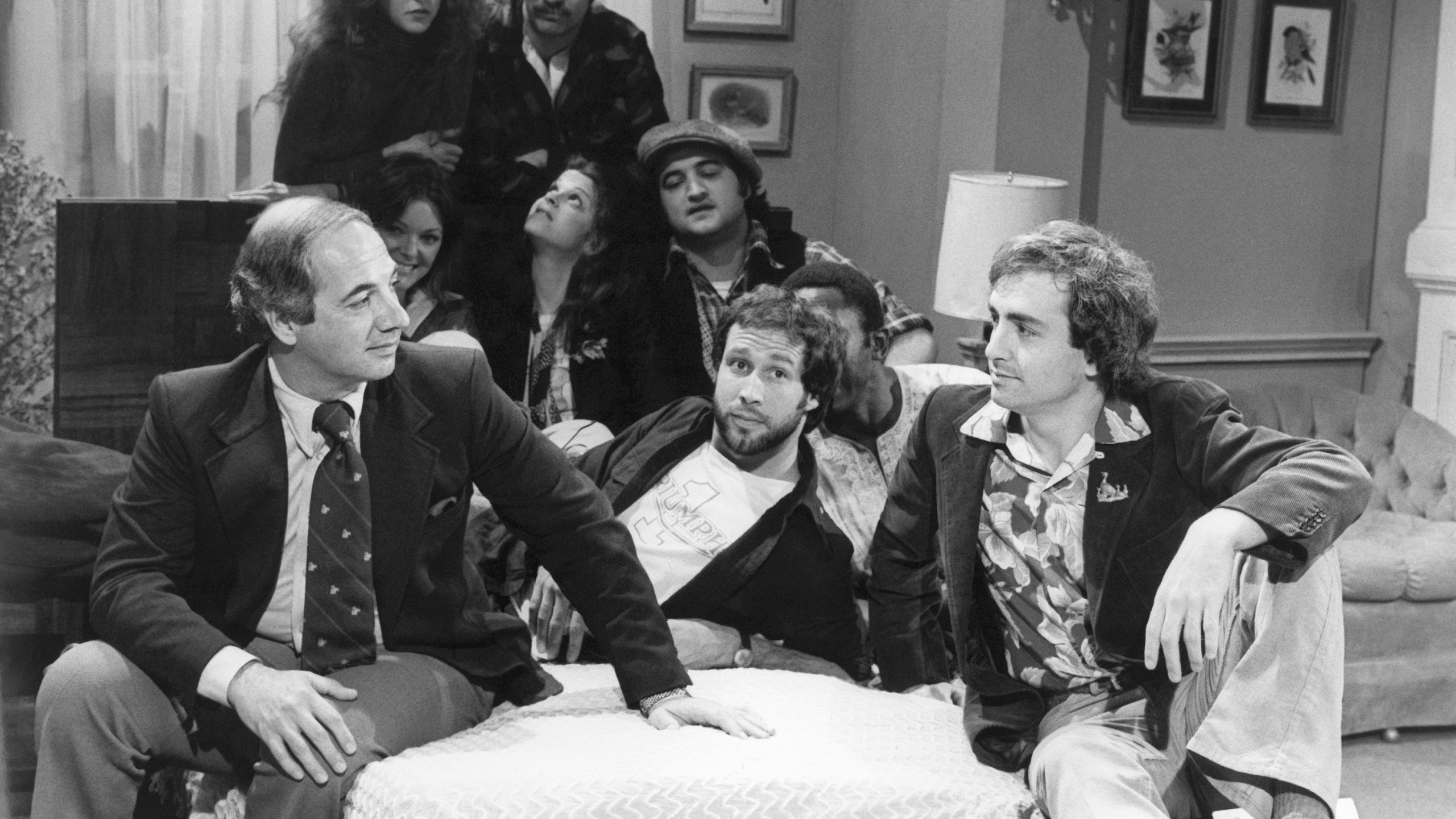 FILE - White House Press Secretary Ron Nessen, left, appears on the "Saturday Night Live" set with producer Lorne Michaels, right, and cast members Chevy Chase, foreground center, Laraine Newman, background left, Dan Aykroyd, background right, Jane Curtin, second row from left, Gilda Radner, John Belushi and Garret Morris, partially obscured, on April 17, 1976, in New York. (AP Photo)