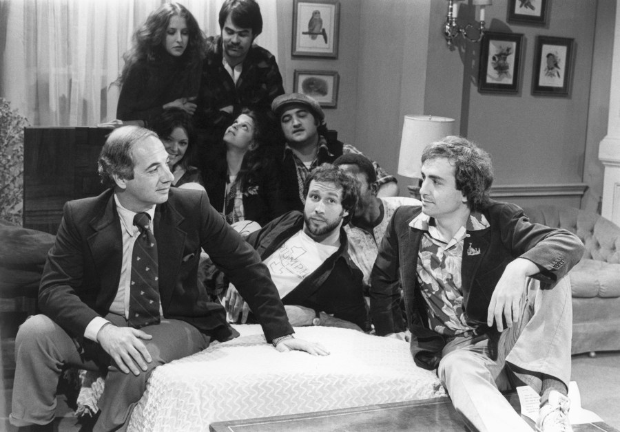 FILE - White House Press Secretary Ron Nessen, left, appears on the "Saturday Night Live" set with producer Lorne Michaels, right, and cast members Chevy Chase, foreground center, Laraine Newman, background left, Dan Aykroyd, background right, Jane Curtin, second row from left, Gilda Radner, John Belushi and Garret Morris, partially obscured, on April 17, 1976, in New York. (AP Photo)