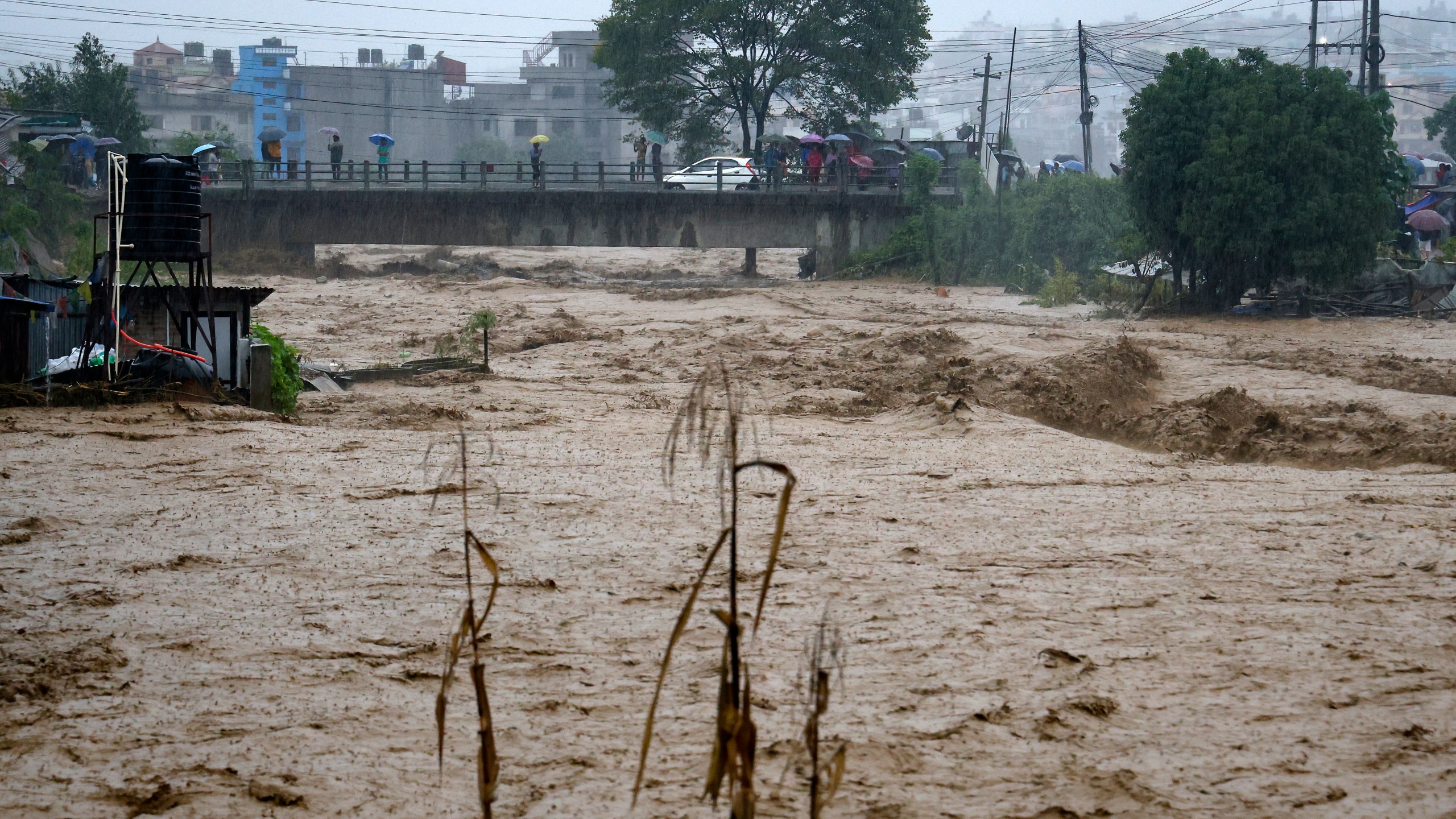 People watch the turbulent waters of Bagmati River from a bridge as the river flooded due to heavy rains in Kathmandu, Nepal, Saturday, Sept. 28, 2024. (AP Photo/Gopen Rai)