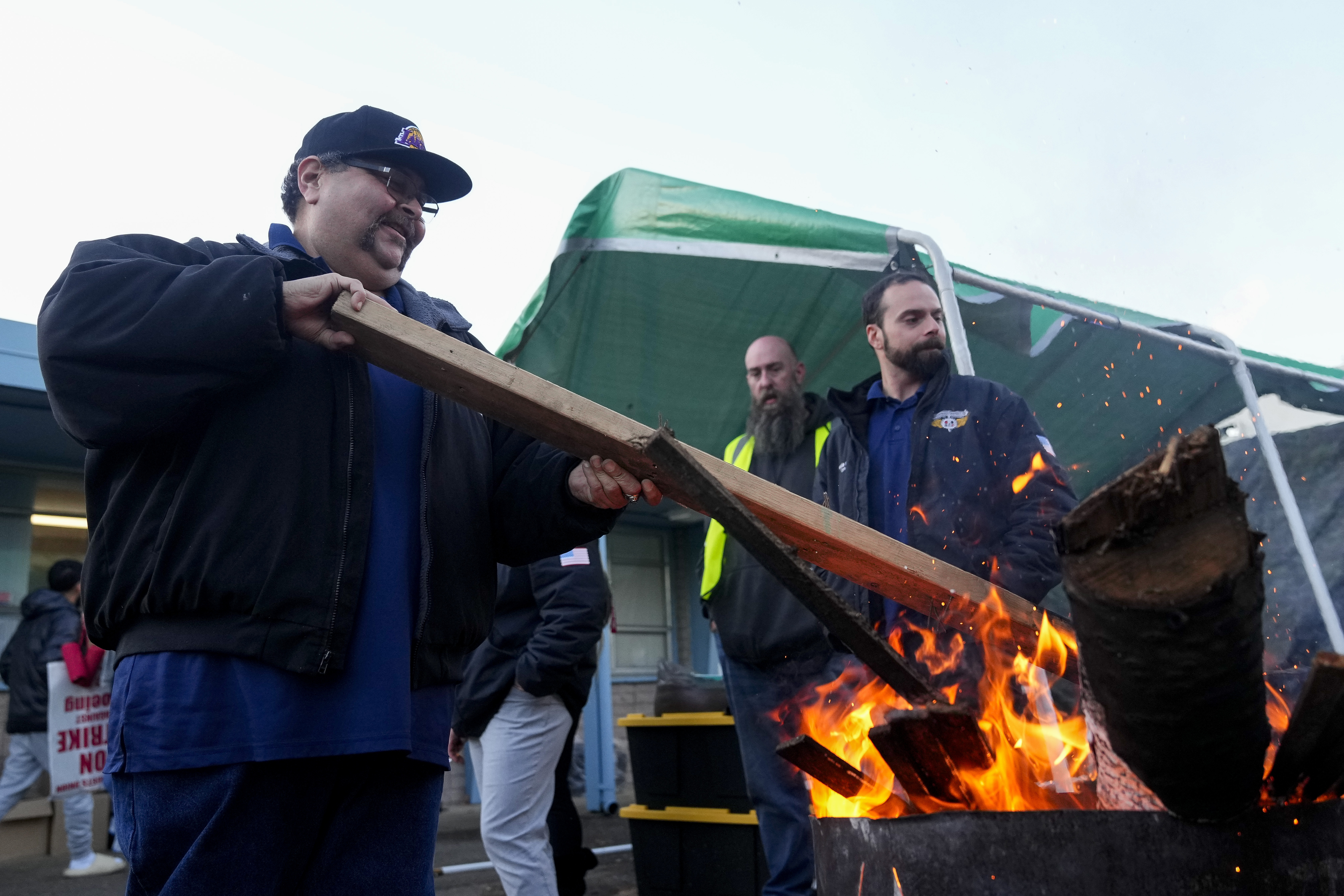 Boeing employee Adrian Camez, who works in Seattle, stokes the fire of a burn barrel as others arrive to vote on a new contract offer from the company Monday, Nov. 4, 2024, at the Aerospace Machinists Union hall in Renton, Wash. (AP Photo/Lindsey Wasson)