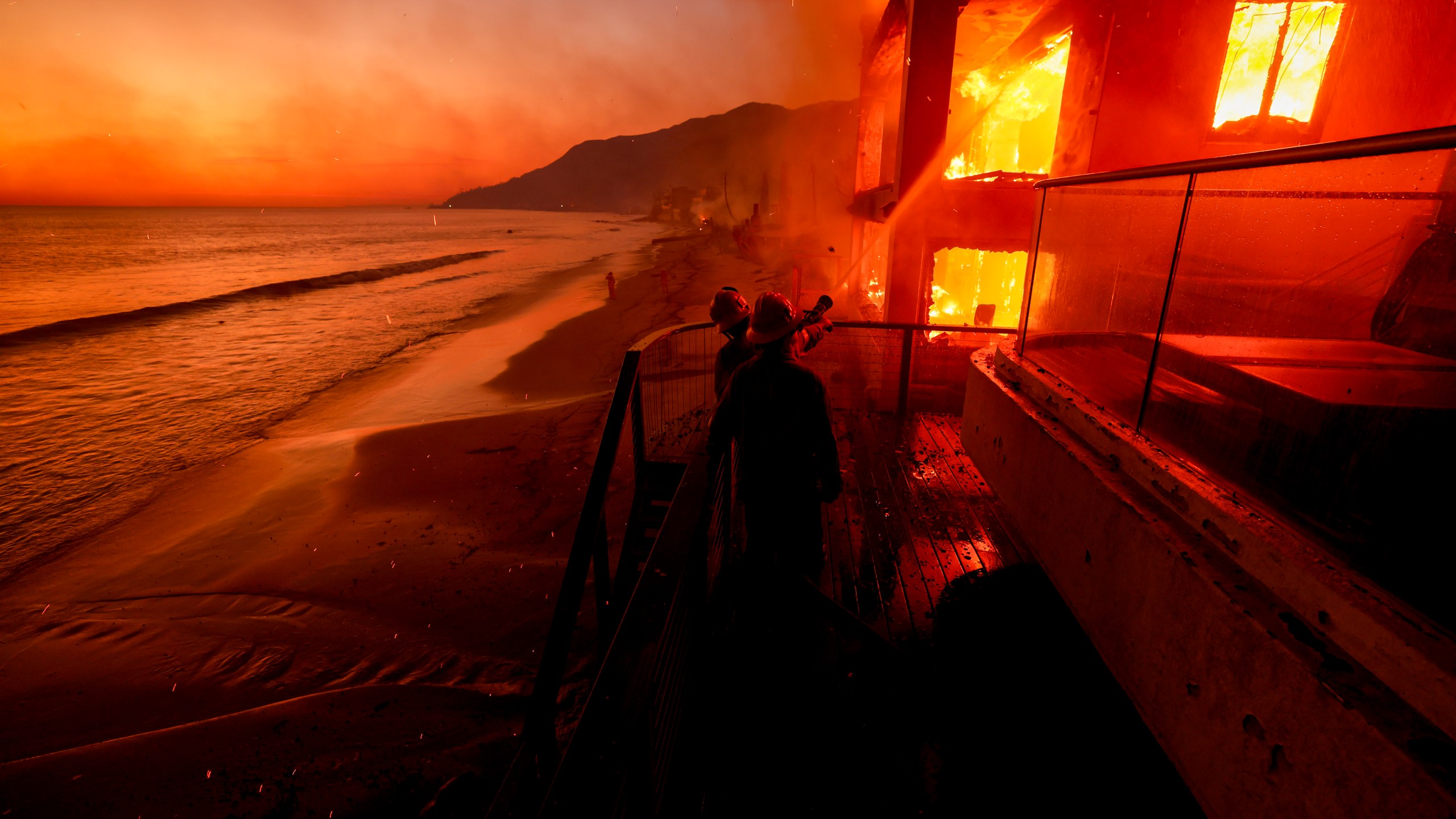 FILE - Firefighters work from a deck as the Palisades Fire burns a beachfront property Wednesday, Jan. 8, 2025 in Malibu, Calif. (AP Photo/Etienne Laurent, File)