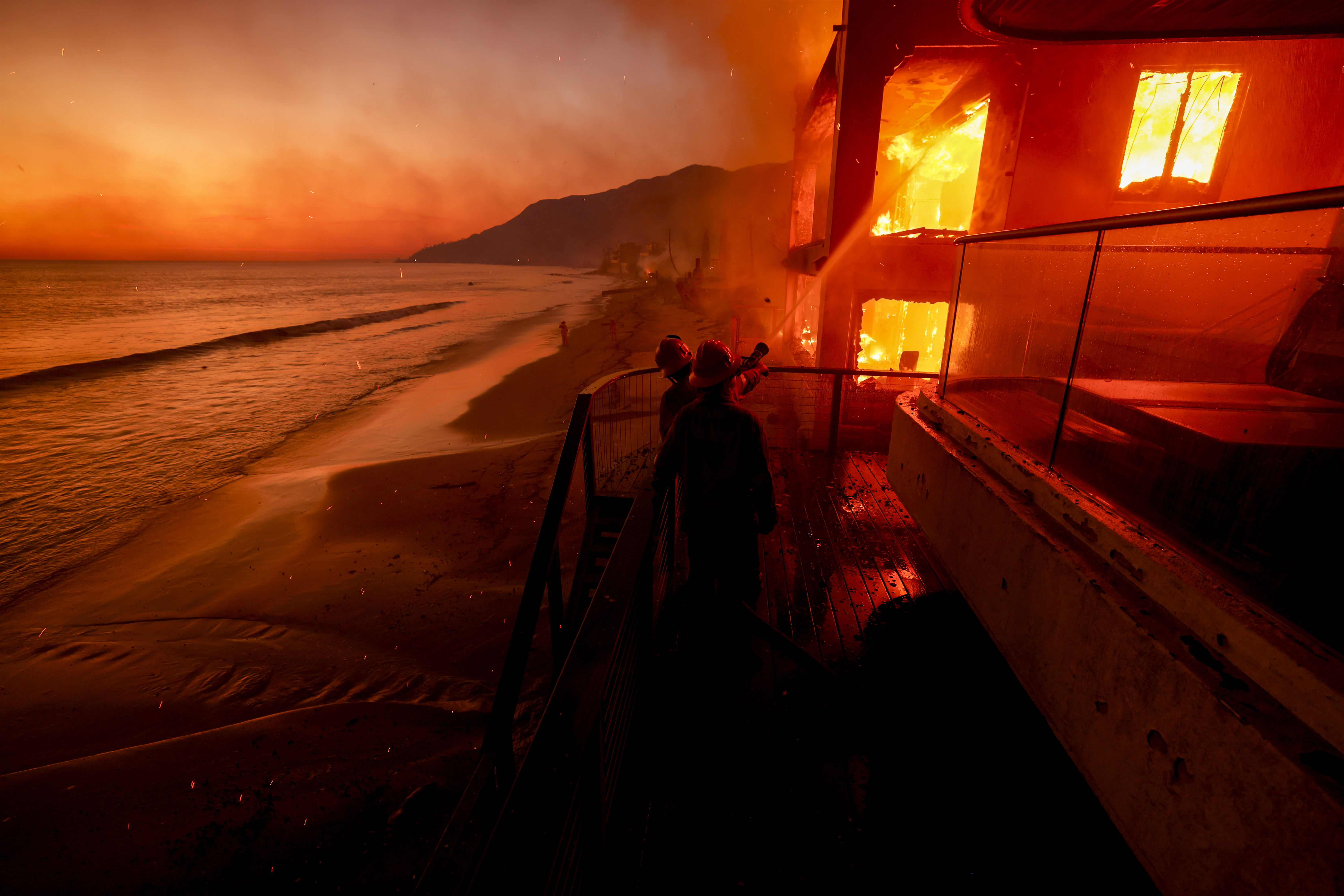 FILE - Firefighters work from a deck as the Palisades Fire burns a beachfront property Wednesday, Jan. 8, 2025 in Malibu, Calif. (AP Photo/Etienne Laurent, File)