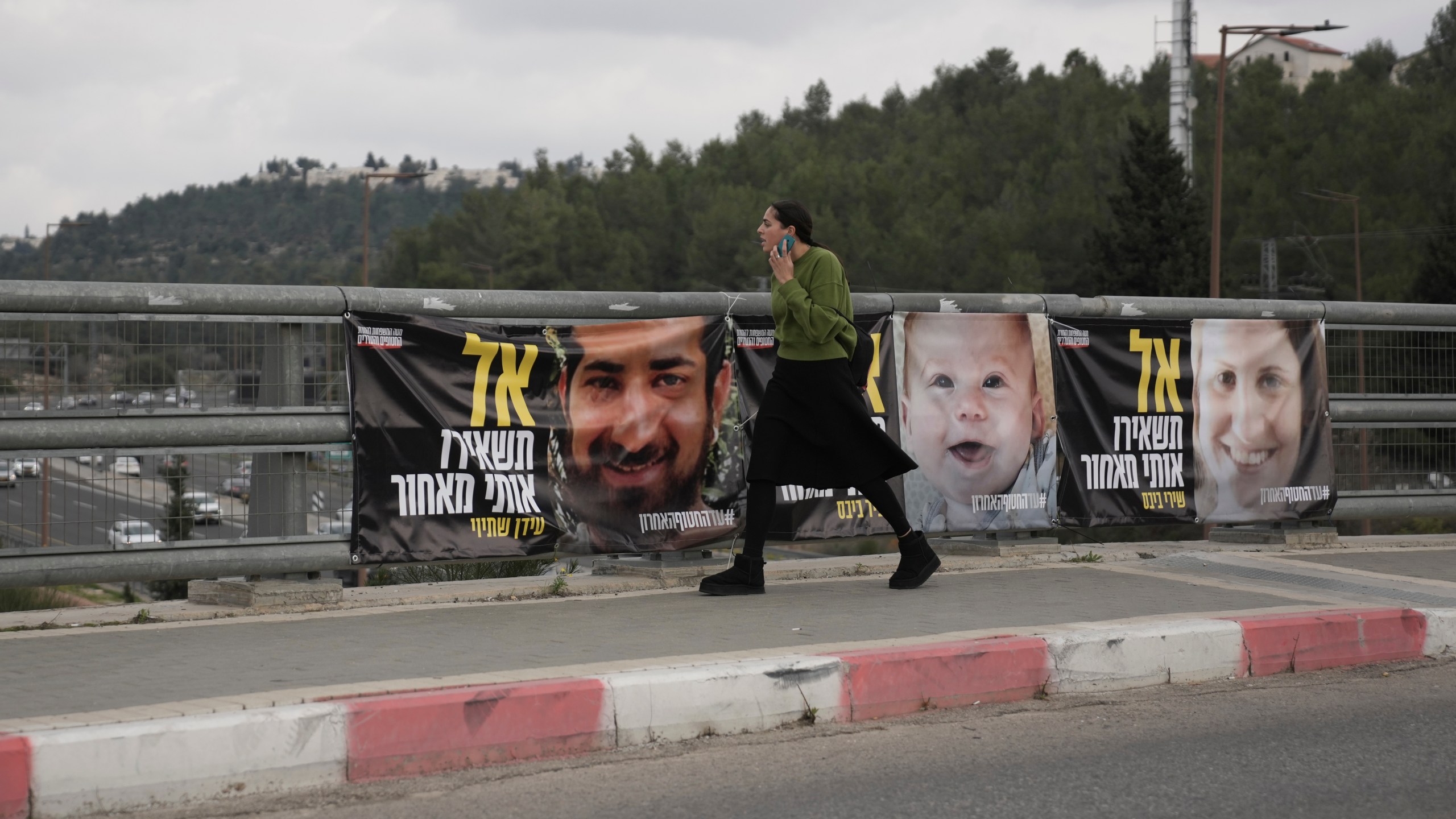 A woman walks past photos of hostages held by Hamas in the Gaza Strip, in Jerusalem, Friday, Jan. 17, 2025. (AP Photo/Mahmoud Illean)