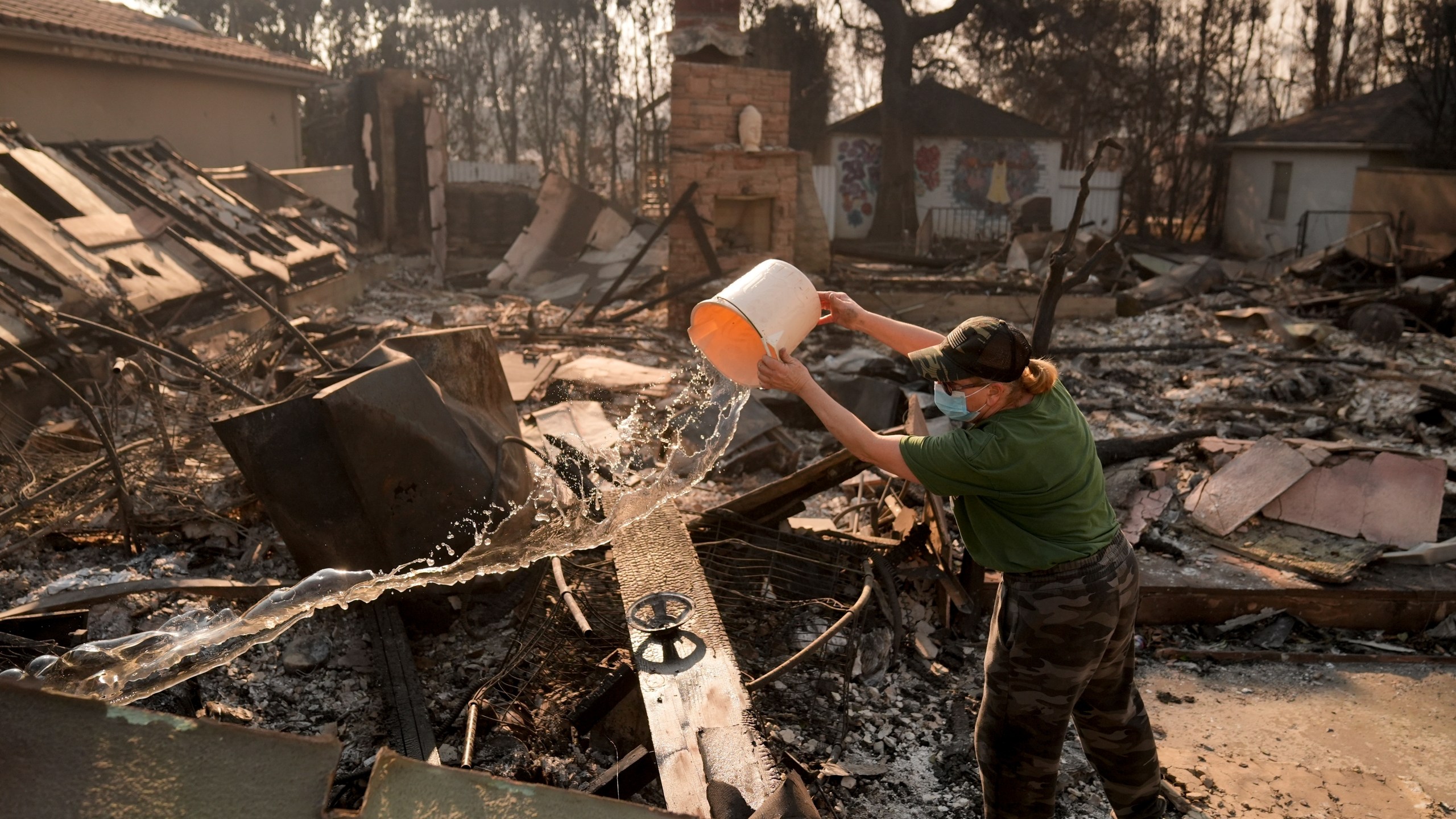 FILE - Nancy Belanger pours water on a neighbor's fire-ravaged property in the aftermath of the Palisades Fire in the Pacific Palisades neighborhood of Los Angeles, Thursday, Jan. 9, 2025. (AP Photo/Jae C. Hong, File)