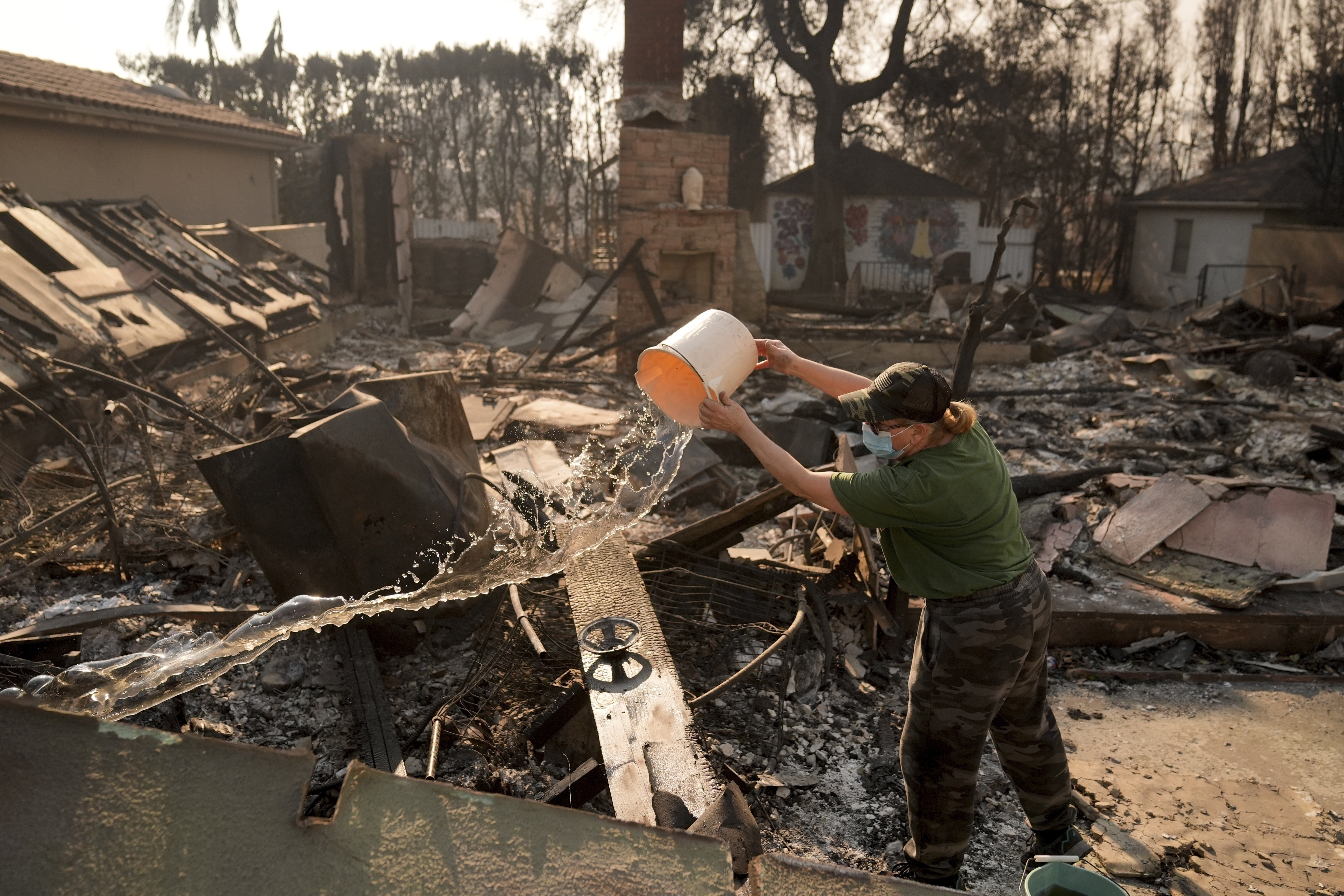 FILE - Nancy Belanger pours water on a neighbor's fire-ravaged property in the aftermath of the Palisades Fire in the Pacific Palisades neighborhood of Los Angeles, Thursday, Jan. 9, 2025. (AP Photo/Jae C. Hong, File)