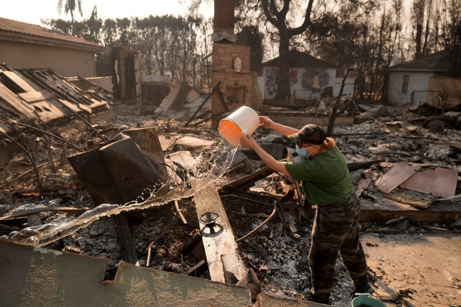 FILE - Nancy Belanger pours water on a neighbor's fire-ravaged property in the aftermath of the Palisades Fire in the Pacific Palisades neighborhood of Los Angeles, Thursday, Jan. 9, 2025. (AP Photo/Jae C. Hong, File)