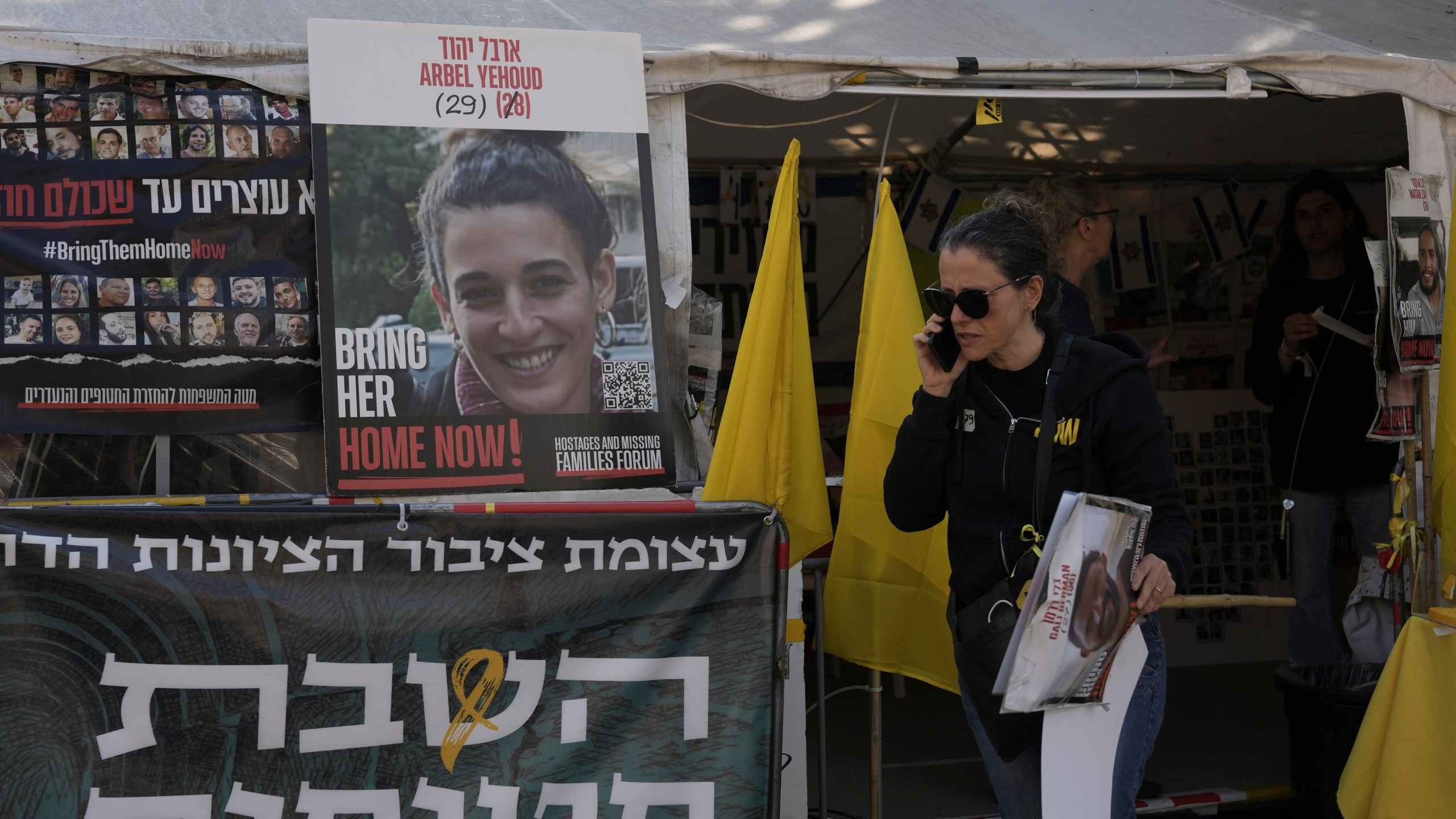 A woman walks past a photo of Arbel Yehoud, and a banner in Hebrew demanding the return of the hostages held by Hamas in Gaza Strip at the entrance of a tent set up in Jerusalem, Monday, Jan. 27, 2025. (AP Photo/Mahmoud illean)