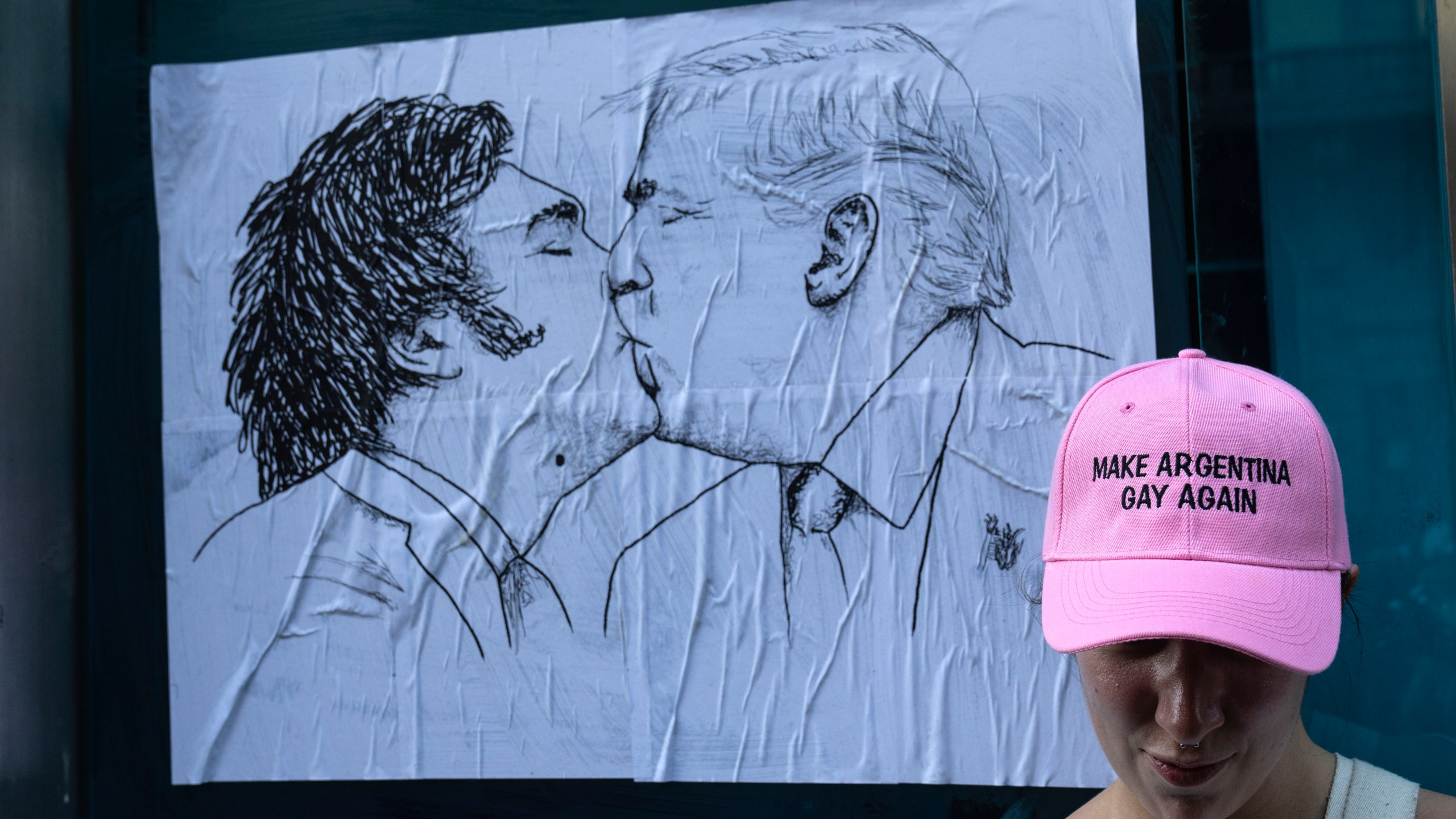 A woman poses for a photo in front of a poster depicting Argentine President Javier Milei and U.S. President Donald Trump sharing a kiss, during a demonstration to protest Milei’s speech at the World Economic Forum in Davos, in which he criticized “sick wokeism,” social welfare, feminism, identity politics and the fight against climate change. (AP Photo/Rodrigo Abd)