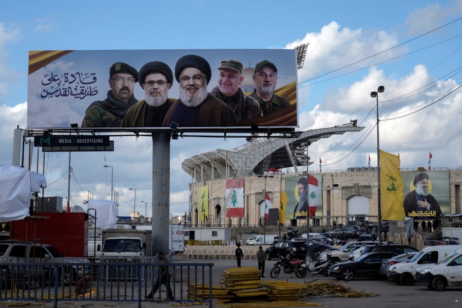 People walk past a billboard with pictures of the late Lebanon's Hezbollah leader Sayyed Hassan Nasrallah, center, late Lebanon's Hezbollah leader Sayyed Hashem Safieddine, second left, Hezbollah top commander Fouad Shukur, left, Hezbollah senior commander Ali Karaki, second right, and Hezbollah commander Ibrahim Akil, right, displayed on Beirut airport highway, Lebanon, Friday, Feb. 21, 2025. (AP Photo/Bilal Hussein)