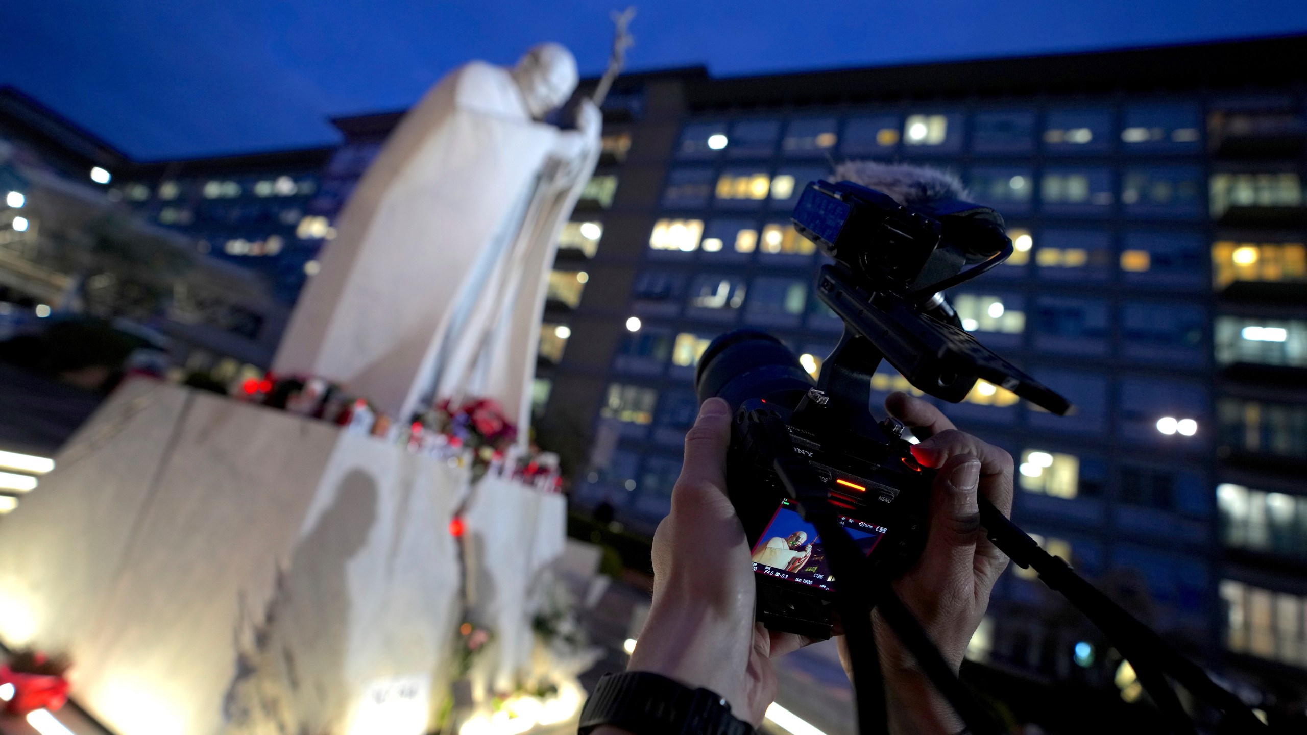 A cameraman scans a marble statue of late Pope John Paul II outside the Agostino Gemelli Polyclinic in Rome where Pope Francis is being treated for pneumonia, Thursday, Feb. 20, 2025. (AP Photo/Domenico Stinellis)