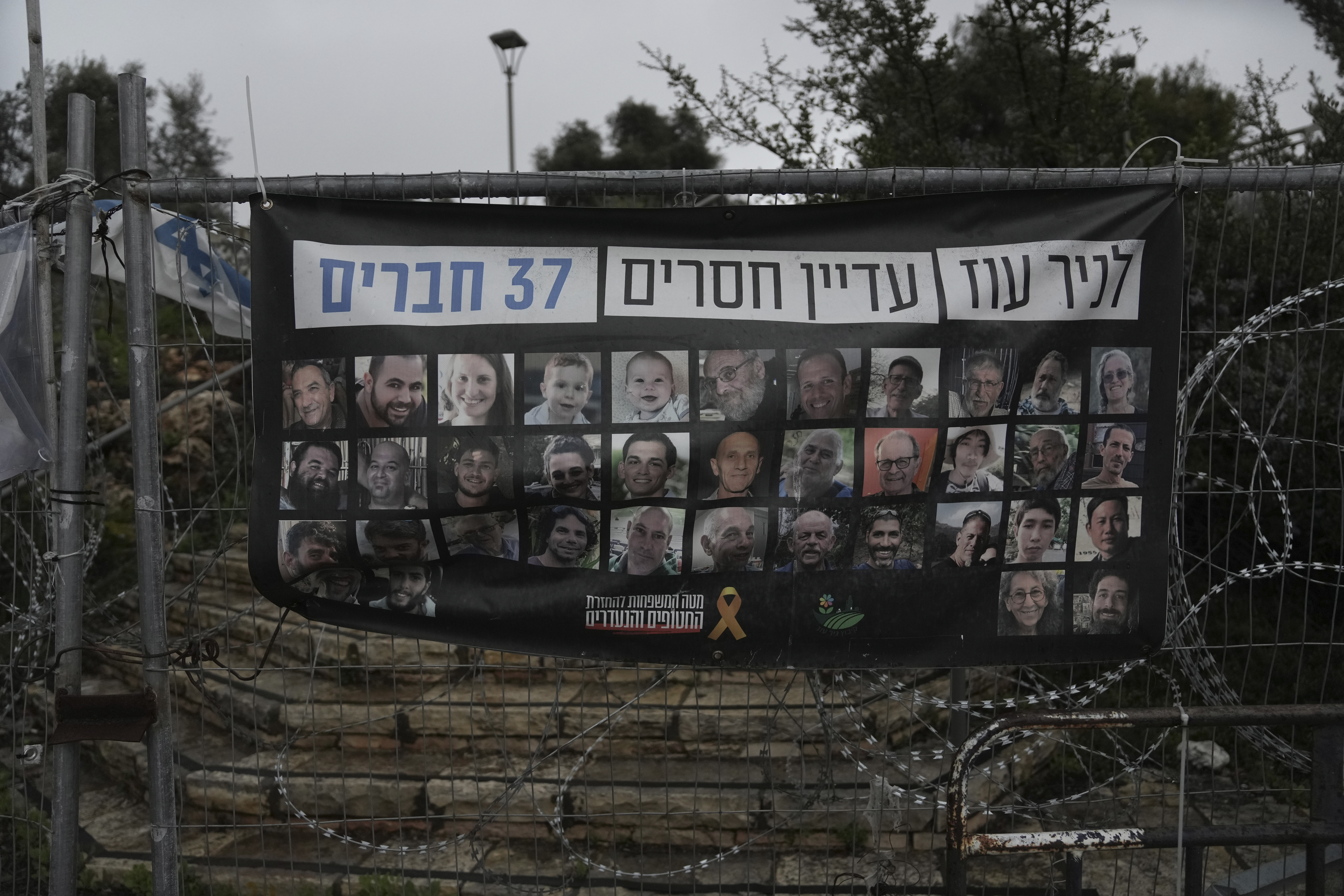 A poster shows portraits of Bibas family, top row from second left: Yarden, Shiri, and their sons Ariel and Kfir, who were kidnapped to Gaza on Oct. 7, 2023, in Jerusalem, Friday, Feb. 21, 2025. Letters on top read, "37 members of Kibbutz Nir Oz are still missing". (AP Photo/Mahmoud Illean)