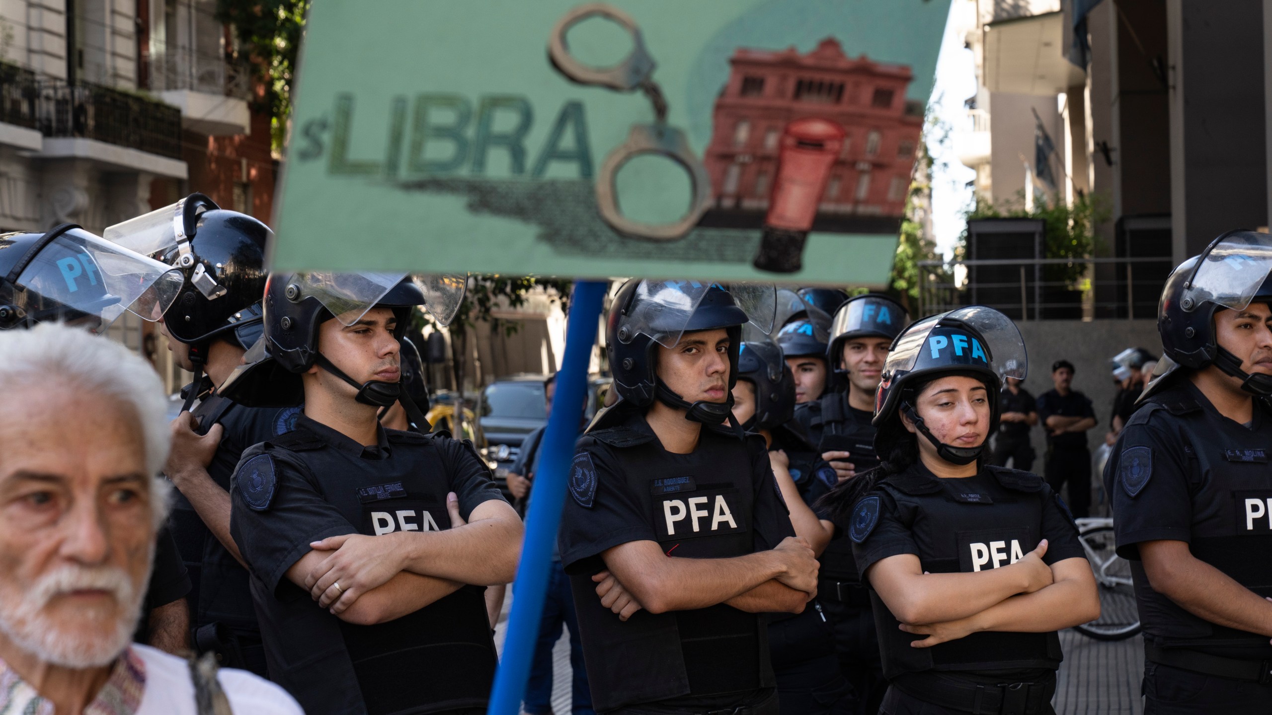 Riot police stand guard as a demonstrator holds a banner depicting the $Libra cryptocurrency during a protest organized by retirees demanding better pensions, in Buenos Aires, Argentina, Wednesday, Feb. 19, 2025. (AP Photo/Rodrigo Abd)