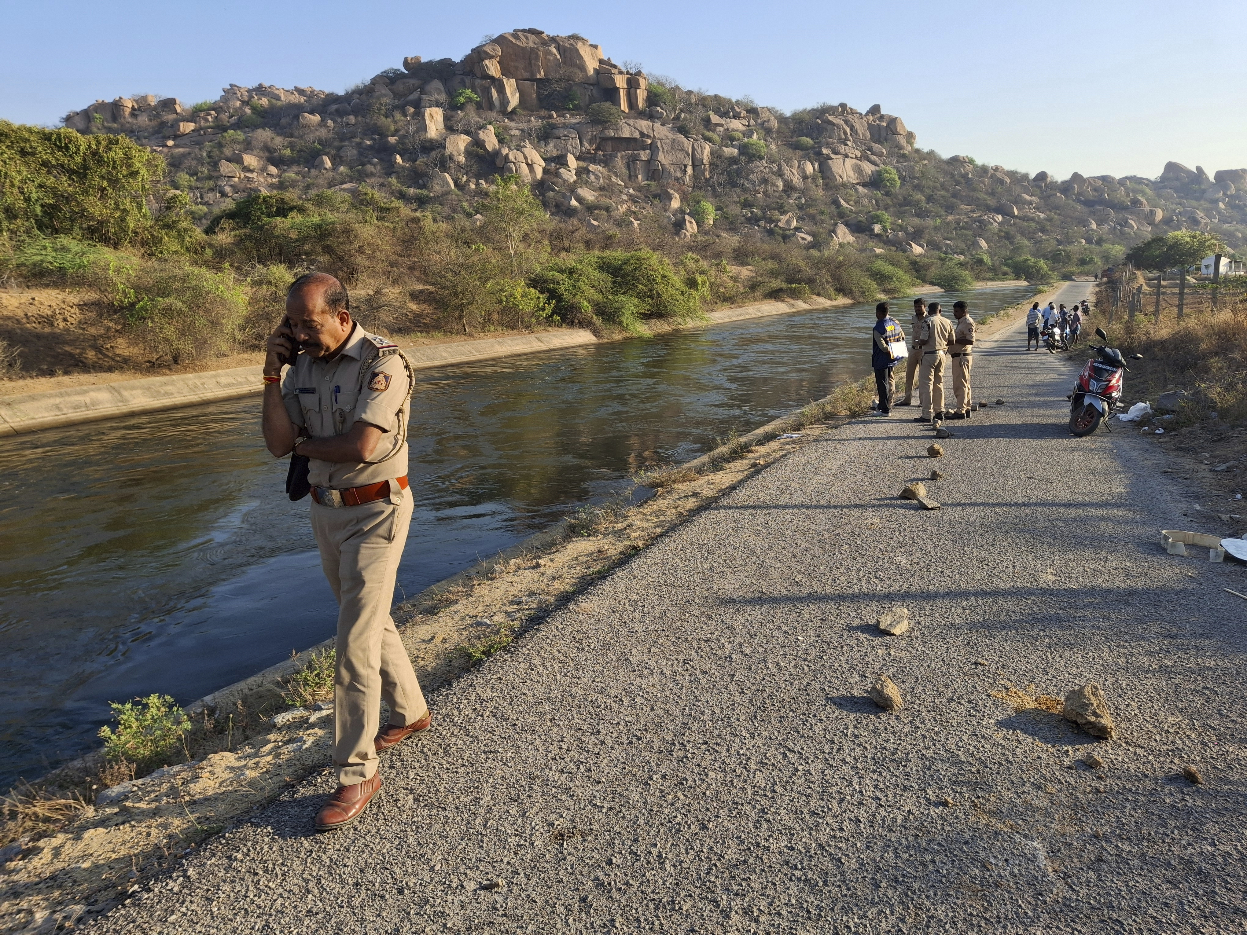 A police officer speaks on his mobile phone at the scene as they search for the male travelers who were pushed into the canal by three men accused of gang-raping two women, in Koppal district of southern state of Karnataka, India, Friday, March 7, 2025. (AP Photo)